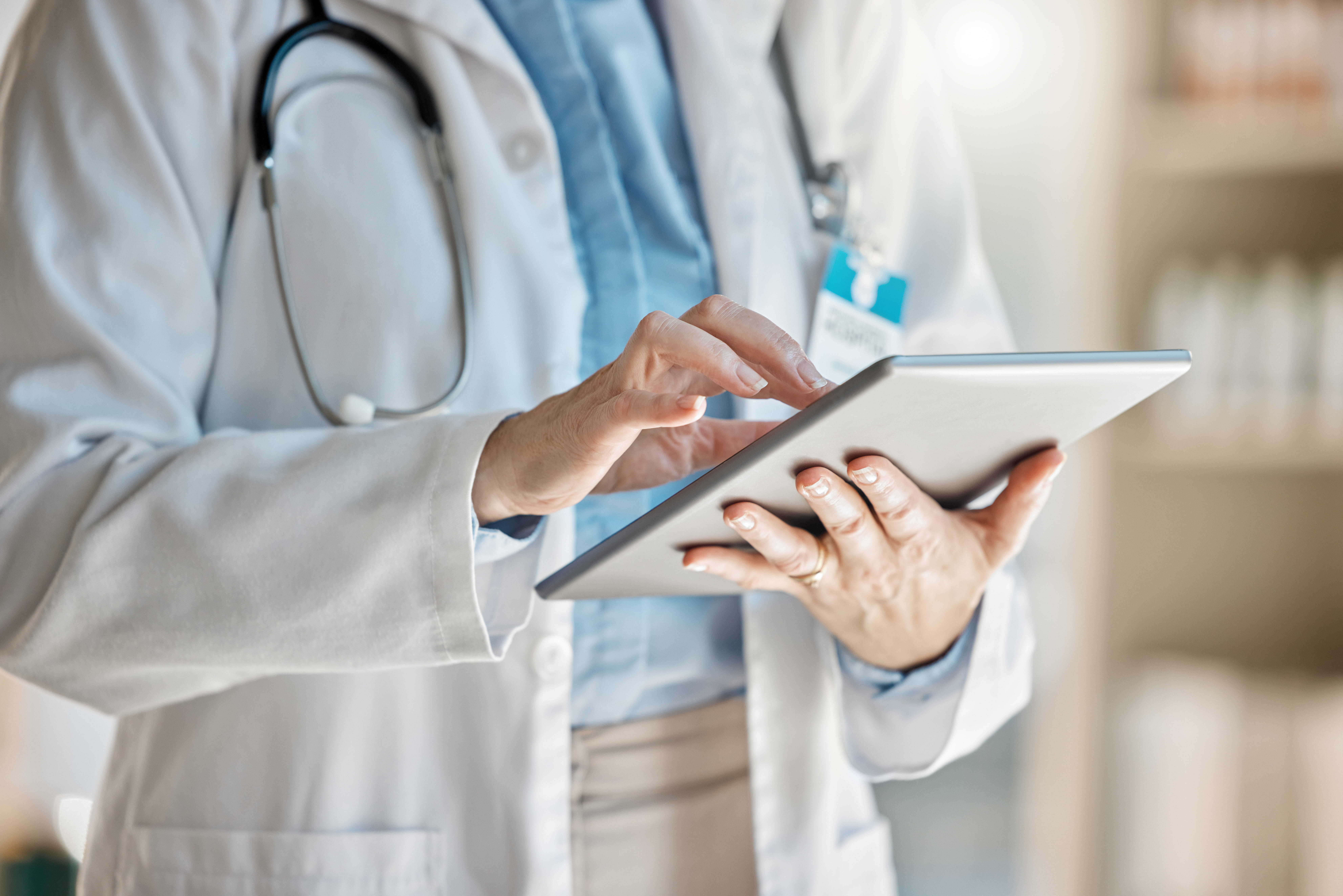 Health professional with a white lab coat and stethoscope using a mobile tablet.