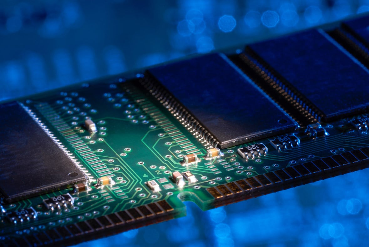 Close-up of a RAM memory module with visible circuitry and chips, lit in blue and green tones.