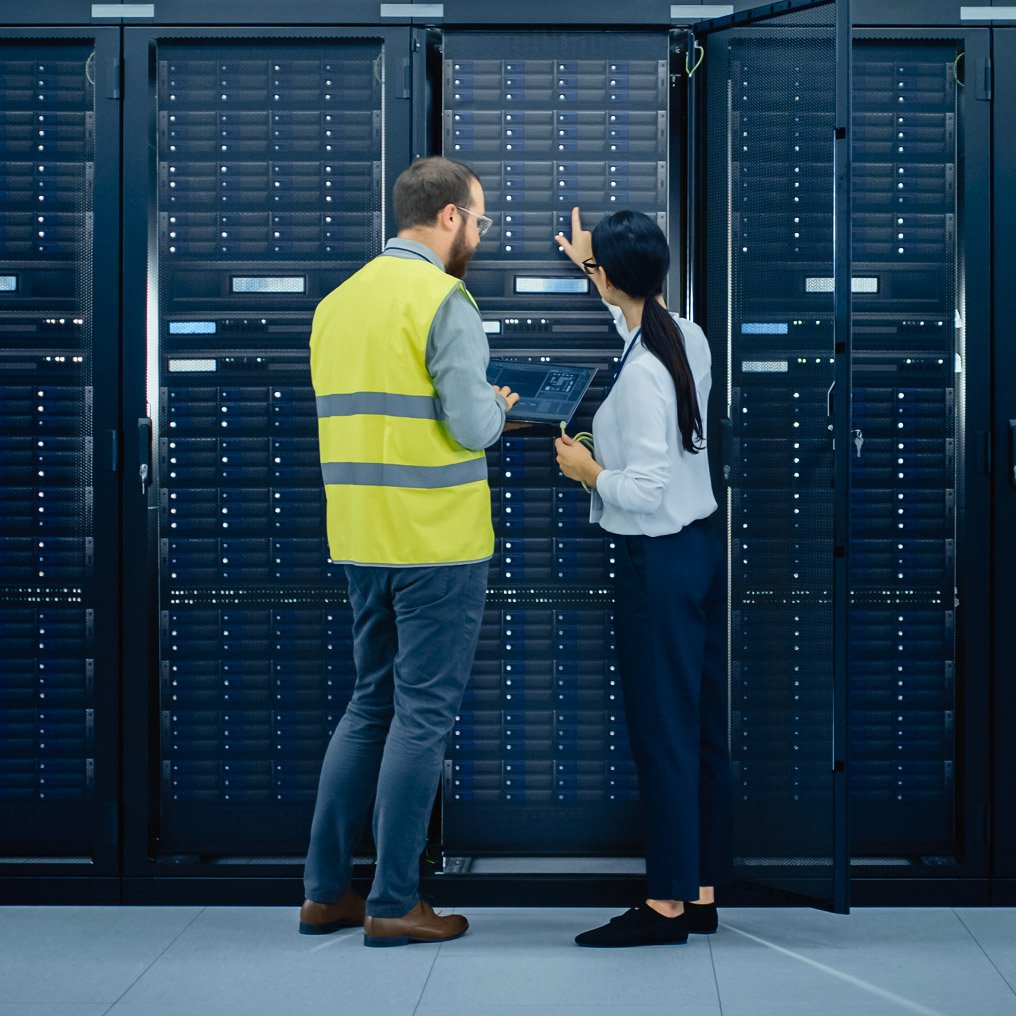 Two people, one in a safety vest, review server hardware