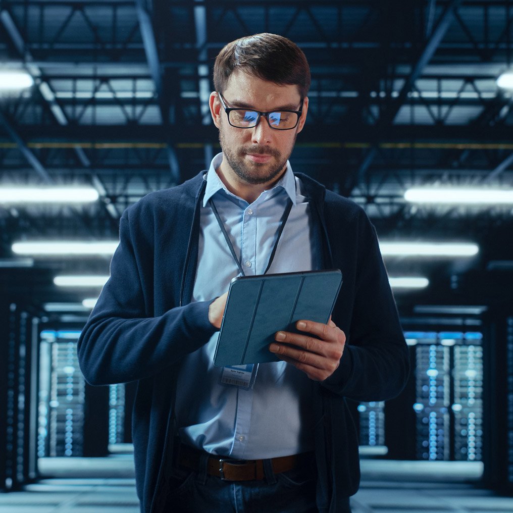 A man views reports on a tablet surrounded by servers