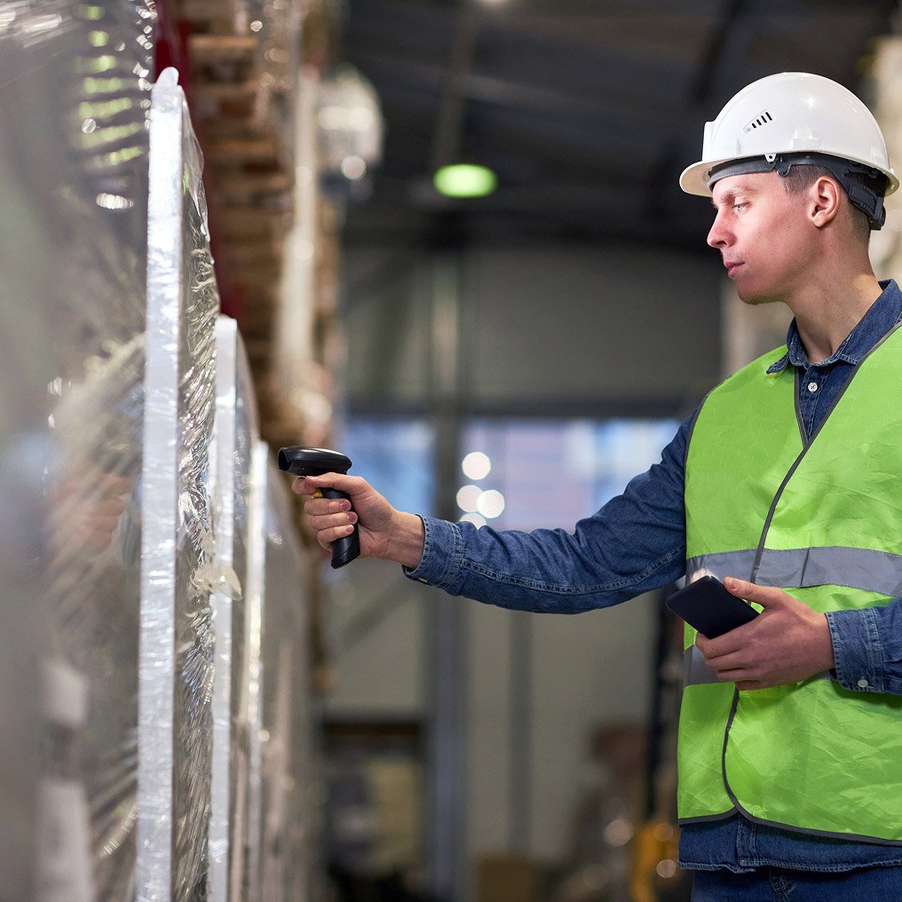 A man in hardhat and safety vest scans a pallet of equipment