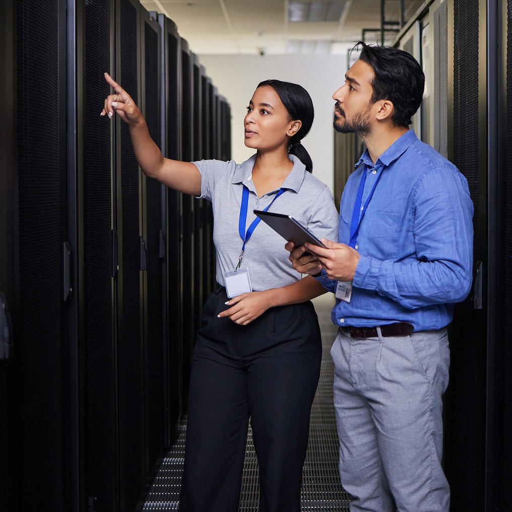 A man and woman inspect servers. He is holding a tablet.