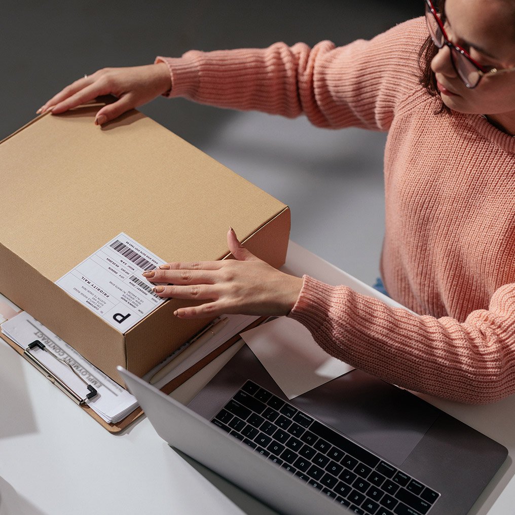 A woman looks at a shipping label while working on a laptop