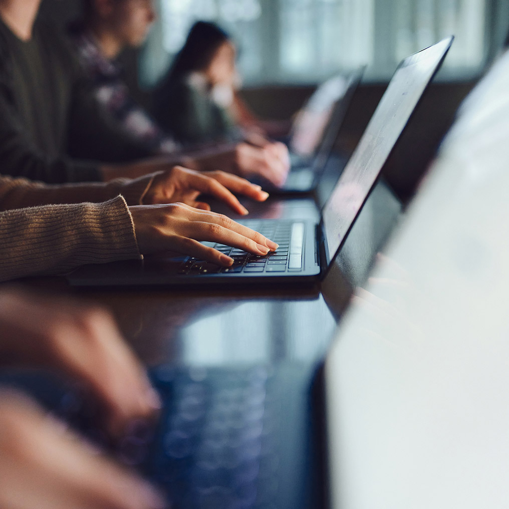 A row of people type on laptop computers