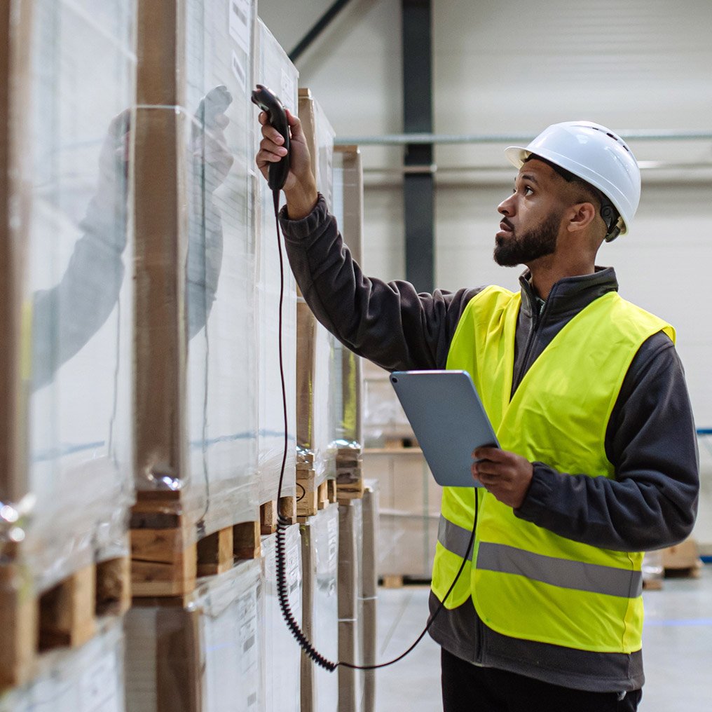 A man in hardhat and safety vest scans a pallet of computer hardware
